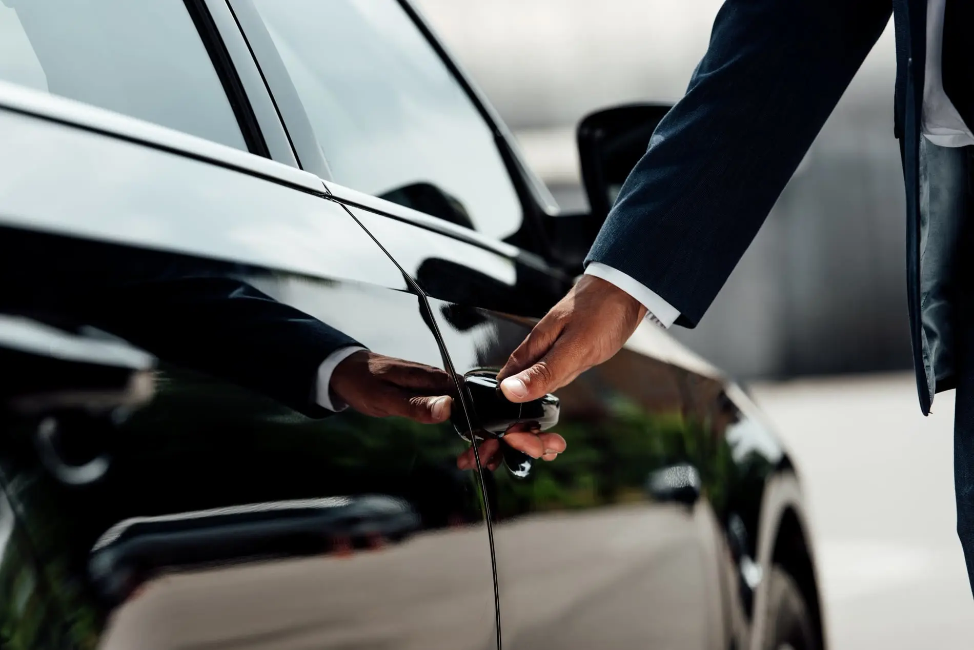 A suited chauffeur opening the door of a black luxury car